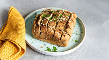 STEINER´s Low Carb High Protein Kastenbrot, eingeschnitten und gefüllt mit Käse. Das Laib liegt auf einem Teller in türkis, daneben ein Geschirrtuch in gelb.