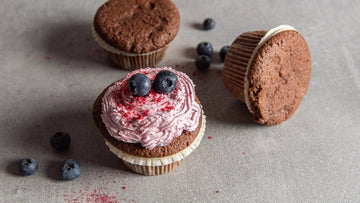 Low Carb Schokomuffins mit einer pinken Creme auf einem grauen Steinuntergrund.