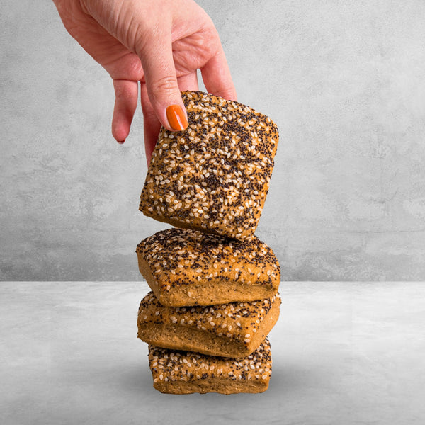 Dreit STEINER´s Low Carb High Proten Saatenbrötchen sind übereinander gestapelt auf einer grauen Fläche. Ein viertes Brötchen wird gerade senkrecht von einer Hand auf den Stapel gehalten. So sind die Saaten zum Betrachter gerichtet.