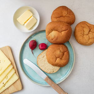 Vier STEINER´s Low Carb High Protein Brötchen liegen auf einem weißen Tisch. Auf einem Teller in Cyan liegt eines der Brötchen aufgeschnitten.