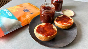 Ein Glas Erdbeermarmelade steht neben einem belegten Brötchen und einer Packung STEINER´s Low Carb Erythrit + Stevia.