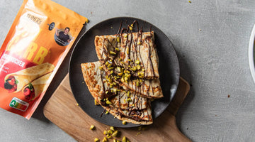 Low Carn Crêpes mit Schokofüllung und gehackten Pistazien liegen auf einem schwarzen Teller.