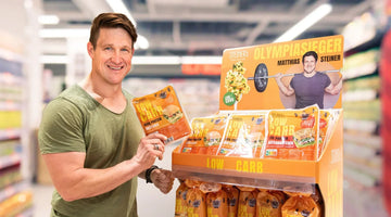 Matthias Steiner steht neben einem STEINER´s Produkt-Display in einem Lebensmittelmarkt. Er hält eine Packung STEINER´s Low Carb Brötchen in die Kamera.
