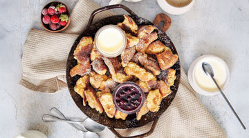 Zubereiteter Kaiserschmarren aus STEINER´s Low Carb Kaiserschmarrn Backmischung in einer gusseisener Pfanne.  Serviert mit Joghurt-Topping und einen Beerenkompott.
