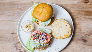 Zwei STEINER´s Burger Buns serviert mit einem Rindfleischpatty, Salat, Tomate und der Low Carb Burgersoße. Die Buns sind auf einem weißen Teller angerichtet.