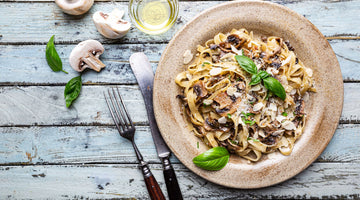 STEINER´s Tagliatelle mit gebratenem Ingwer-Gemüse. Angerichtet auf einem braunem Teller. Neben dem Teller befinden sich aufgeschnittene weiße Champignons und vintage-Besteck.