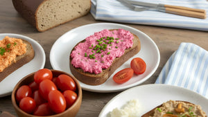 Eine Schreibe STEINER´s Brot mit einem Radieschen-Aufstrich liegt auf einem wißen Teller. Der Teller staht auf einem blau weiß gestreiften Tuch. Zu sehen ist ein Holztisch, ein Laib STEINER´s Brot.