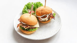 Zwei Burger mit STEINER´s Burger Buns, Rindfleichpatty, Speck, Bergkäse und Zwiebeln auf einem weißen Teller.