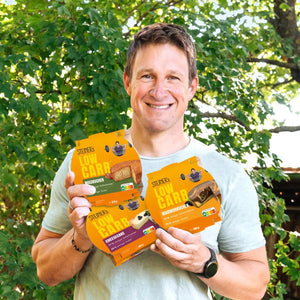 Matthias steht in der Natur und hält drei Packungen STEINER´s Low Carb Kuchen in den Händen.