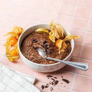 Eine Schüssel mit zubereitetem STEINER´s Low Carb Schoko Porridge steht auf einem orangefarbenen Untergrund.  Der Porridge wurde mit zwei Physalis dekoriert. Links daneben liegen ebenfalls zwei Physalis zur Dekoration.