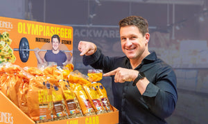 Matthias Steiner zeigt auf einen Produktaufsteller, der mit STEINER´s Produkten gefüllt ist.