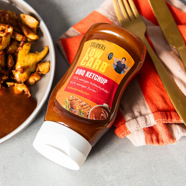 Eine Flasche STEINER´s Low Carb BBQ Ketchup neben einem Teller mit gebratenem Fleisch und einem Belagensalat.