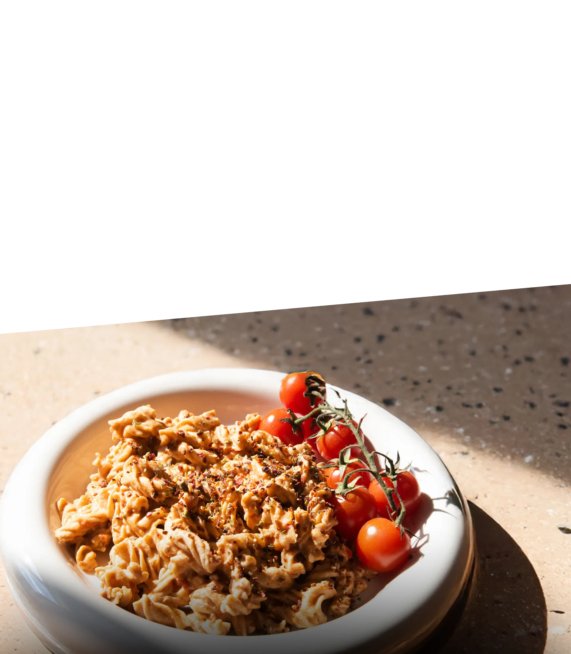 Zubereitete STEINER´s Low Carb High Protein Fusilli mit einer Tomaten-Sahne-Soße auf einem runden Teller.