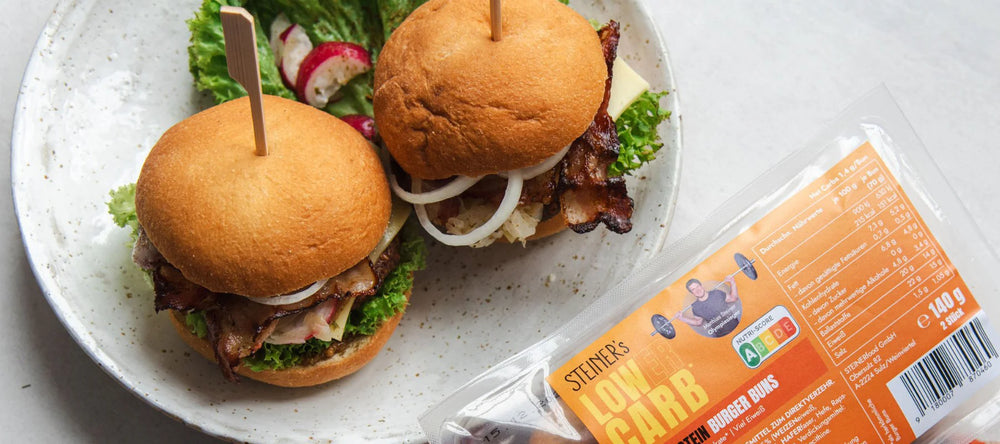 Auf einem Holzbrett liegt ein ganzes STEINER´s Low Carb High Protein Brötchen und zwei Brötchenhälften belegt mit Bruschetta. Dahinter ist eine Schale mit Bruschetta zu sehen.