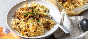 STEINER´s Low Carb Locken-Spätzle als Käsespätzle serviert auf einem Keramikteller, mit Silberlöffel, Pfeffermühle und die Auflaufform sind rechts zu sehen