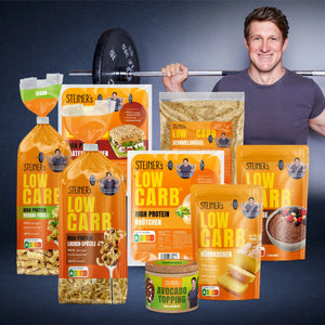 STEINER´s Kennenlern Deal Box mit Low Carb Produkten wie Nudeln, Brötchen und Gewürz. Matthias Steiner ist mit Hantelstange ist im Hintergrund.