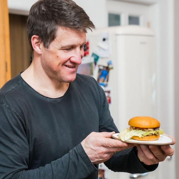 Der Olympiasieger im Gewichtheben betrachtet einen zubereiteten Burger aus STEINER´s Low Carb High Protein Burger Buns.