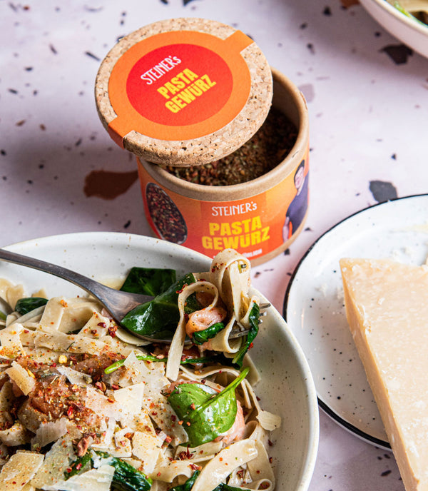 STEINER´s Low Carb High Protein Tagliatelle zubereitet mit einer Soße aus Sahne, Spinat und Lachs getoppt ist das Gericht mit STEINER´s Pasta Gewürz. Die Pasta ist auf einem weißen Teller serviert. Daneben steht eine Dose STEINER´s Pasta Gewürz.