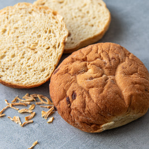 Ein ganzes STEINER´s Zwiebelbrötchen und ein aufgeschnittenes STEINER´s Zwiebelbrötchen liegen auf einem grauen Steinuntergrund. Daneben ein paar Röstzwiebeln, die in den Zwiebelbrötchen eingebacken wurden.